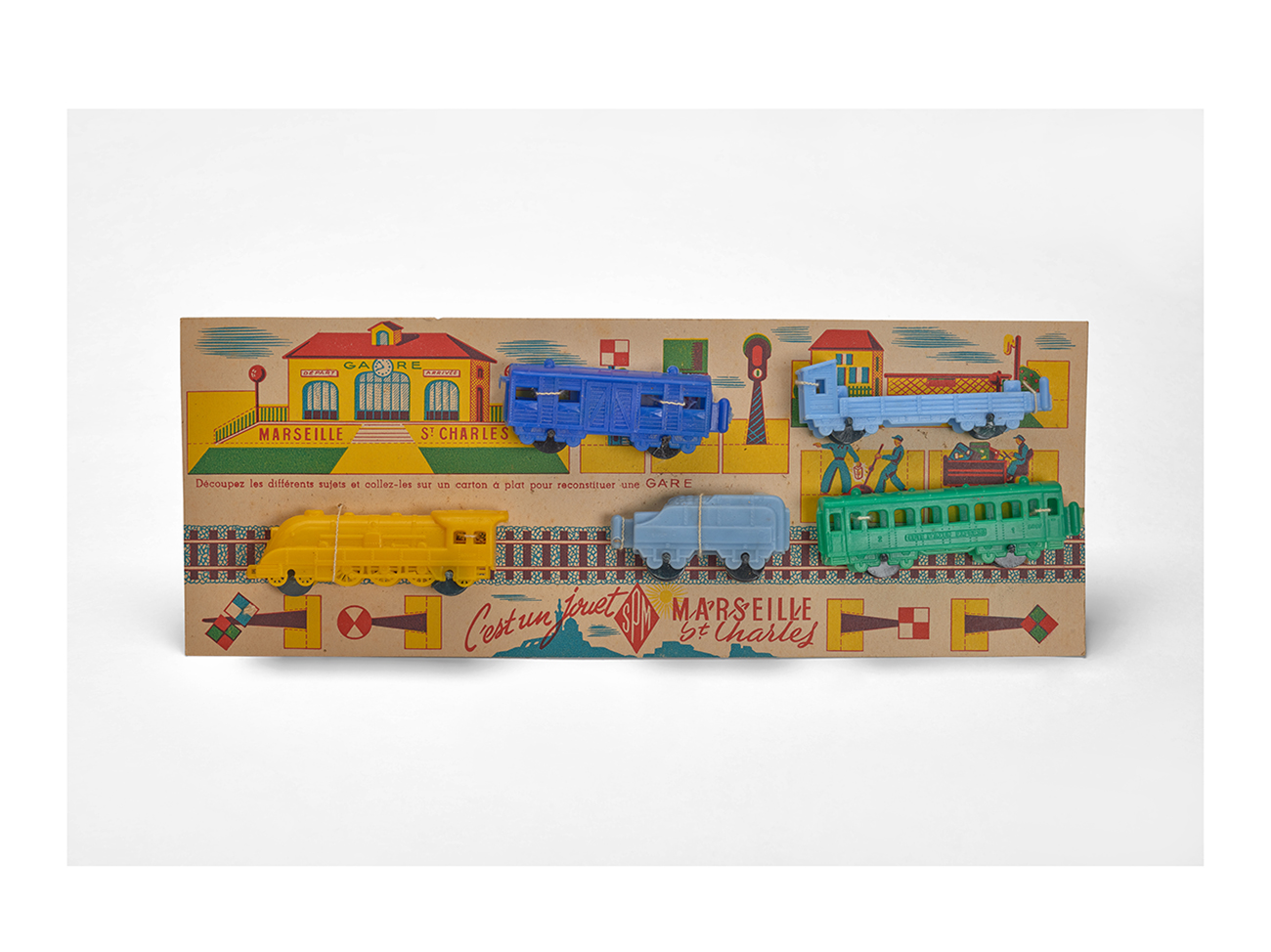 “Marseille St-Charles” locomotive and its carriages fixed on a cardboard station set, manufactured by SPM, 1950s. Plastic train, cardboard box. Massilia Toy, Marseille © Yves Inchierman